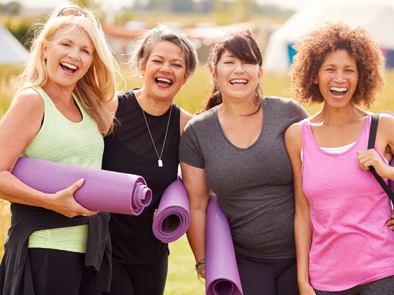 A portrait of a group of mature female friends, smiling at the camera, carrying yoga mats.